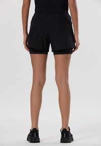 Pantalones cortos deportivos negros con una capa interior ajustada, cinturilla elástica y aberturas laterales para mayor movilidad. Combinados con zapatillas de correr negras.