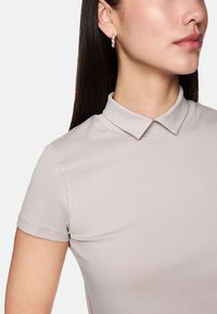 Light beige polo shirt with a collar, short sleeves, and smooth texture. Includes visible stitching along the collar and sleeves.