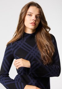 Jersey de punto en negro y azul oscuro con una textura acanalada y un patrón geométrico. Cuello alto y mangas largas; silueta ajustada.