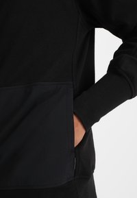 Felpa nera con un corpo in pile testurizzato e una tasca in materiale liscio a contrasto, con polsini e orlo a costine.