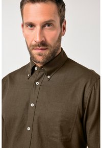 Braunes Hemd mit Knopfleiste aus strukturiertem Stoff, mit aufgesetzter Tasche, klassischem Kragen und weißen Knöpfen vorne.