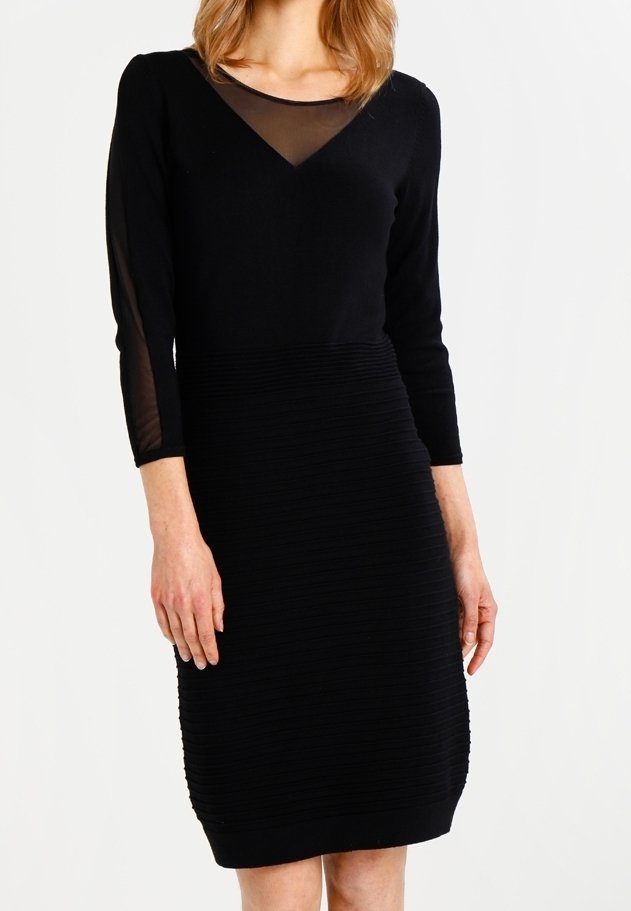 Robe noire avec une partie inférieure ajustée et côtelée et un haut lisse. Des manches longues transparentes et un décolleté en V accentuent le design.