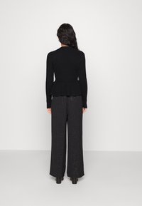 Fekete bordás pulóver peplum derékkal, széles lábú fekete nadrággal párosítva, amely diszkrét csillogó textúrával rendelkezik.