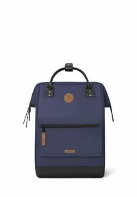 Zaino navy con forma rettangolare, dotato di dettagli in pelle nera, tasca frontale con zip e patch del logo marrone. Superficie inferiore testurizzata.