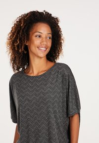 Grå kortærmet top med et fiskebensmønster, der har en rund halsudskæring og løs pasform, lavet af et tekstureret stof.