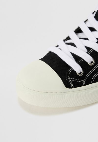 Schwarze Leinenschuhe mit weißen Schnürsenkeln, Gummikappe und kontrastierenden Nähten. Verfügt über eine strukturierte Sohle und glatte Akzente.