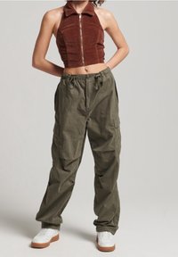 Brauner Corduroy-Top mit hohem Kragen und Reißverschluss vorne, kombiniert mit lockeren olivgrünen Cargo-Hosen und weißen Sneakern.