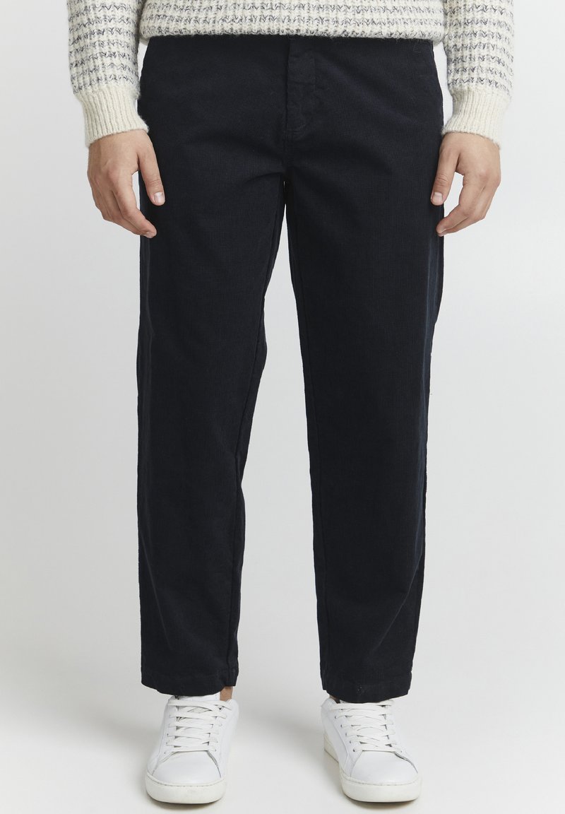 Donkerblauwe corduroy broeken met een ontspannen pasvorm, voorzien van zijzakken en een soepele textuur, gecombineerd met witte sneakers.