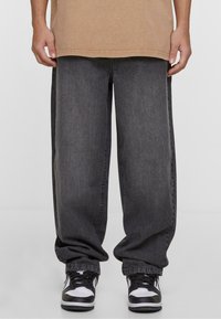 Jeans de pierna ancha en gris oscuro con una textura desvaída, con costuras laterales y tobillos remangados, combinados con zapatillas negras y blancas.