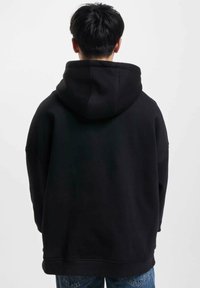 Black hooded sweatshirt viewed from the back, featuring a loose fit, ribbed hem, and soft fabric texture.