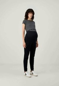Maternity outfit featuring a striped short-sleeve top and dark joggers, complemented by white sneakers with black accents.