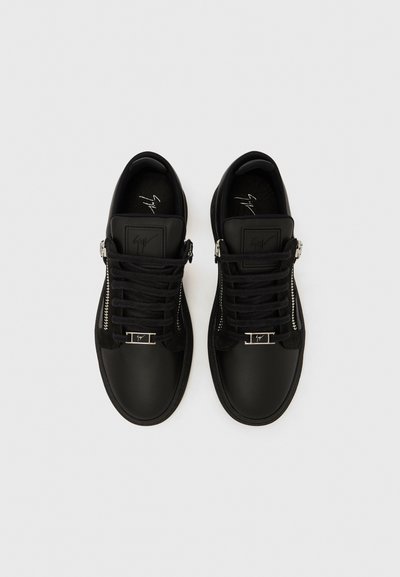 Pair of black leather sneakers with side zippers, black laces, and silver logo accents on white background, viewed from above.