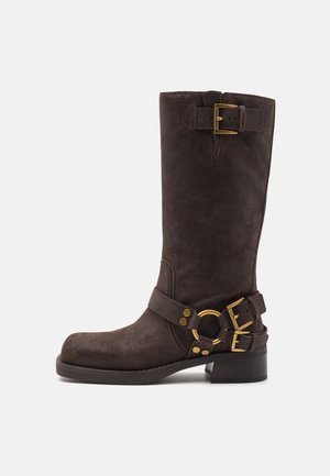 Botte mi-mollet en daim marron foncé avec boucles dorées, bout rond, talon bloc bas et bride avec détail anneau autour de la cheville.