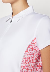 Weißes Polohemd mit Reißverschluss, das ein weiches, pinkfarbenes Leopardenmuster an der Seitenpartie aufweist. Kurzärmlig und mit strukturiertem Kragen rundet es das Design ab.