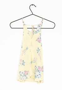 Żółta sukienka w kwiaty z dekoltem w kształcie litery V i regulowanymi ramiączkami, z różowymi i niebieskimi wzorami kwiatowymi. Wisząca na czarnym metalowym wieszaku.