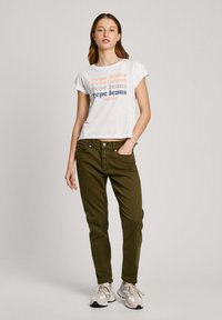 Bijela skraćena majica s višebojnim natpisom "Pepe Jeans"; maslinasto zelene uske hlače; sivi i bijeli tenisice; jednostavan dizajn i ležeran stil.