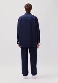 Marineblaue Jeanshemd mit lockerer Passform, Knopfmanschetten und abgerundetem Saum, kombiniert mit passenden, locker sitzenden Hosen und weißen Turnschuhen.
