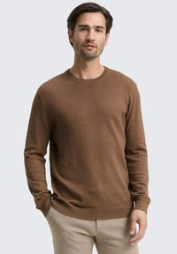Brauner Strickpullover mit Rundhalsausschnitt und langen Ärmeln, der eine glatte Textur und eine eng anliegende Passform aufweist, kombiniert mit hellen Hosen.