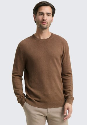 Brauner Strickpullover mit Rundhalsausschnitt und langen Ärmeln, der eine glatte Textur und eine eng anliegende Passform aufweist, kombiniert mit hellen Hosen.