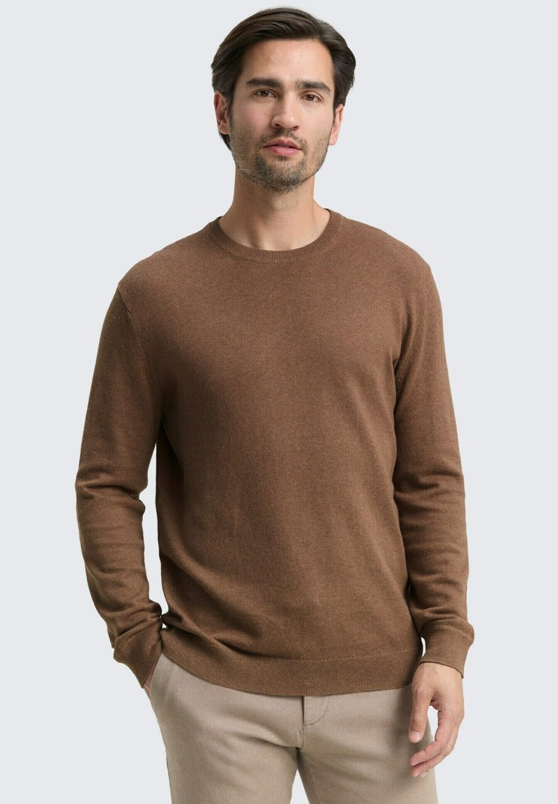 Brauner Strickpullover mit Rundhalsausschnitt und langen Ärmeln, der eine glatte Textur und eine eng anliegende Passform aufweist, kombiniert mit hellen Hosen.