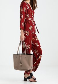 Punane lillemustriga kattesärk laiade varrukatega, koos vastavate pükste ja beeži käekotiga, millel on must äär ja pikad rihmad, ning lamedad mustad sandaalid.