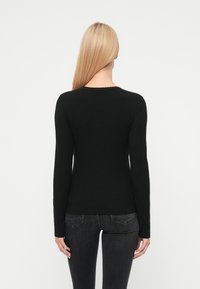 Bluza neagră cu mâneci lungi, cu dungi, cu decolteu rotund și tiv ondulat. Textură moale, design mulat. Asortată cu blugi închiși la culoare.