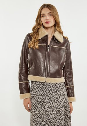 Giacca cropped in pelle marrone con colletto e polsini in shearling, dotata di zip sul davanti, dettagli in borchie e rifiniture in shearling di colore crema.