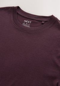 T-shirt in cotone di colore viola scuro con scollo rotondo, taglio regolare ed etichetta con indicazioni su misura e cura. Texture liscia, senza motivi.