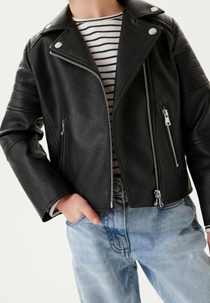 Sort faux læder bikerjakke med sølvfarvede lynlåse, trykknapkrave og ribbede skulderdetaljer, båret over en stribet skjorte og lyseblå jeans.