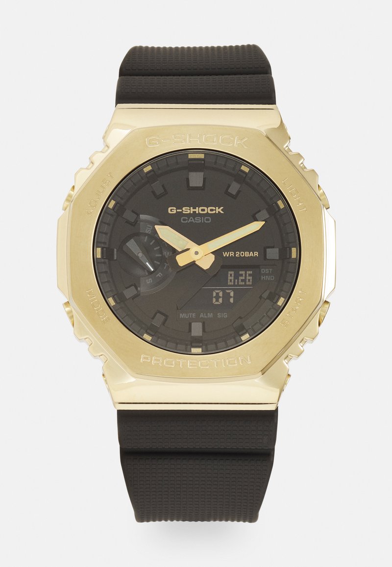 Montre G-Shock avec un cadran noir, boîtier doré et bracelet en caoutchouc noir. Les caractéristiques incluent un écran numérique et des accents de surface texturée.