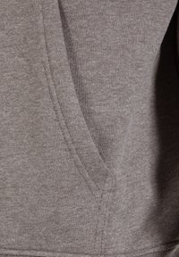 Brun sweatshirtstof med en blød tekstur, en sidelomme og synlig syning. Designet er enkelt og funktionelt.