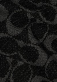 Melnā un pelēkā teksturētā adīta auduma ar apaļu rakstu, kurā ir dažādi dziļumi, radot vizuālu interesi materiālā.