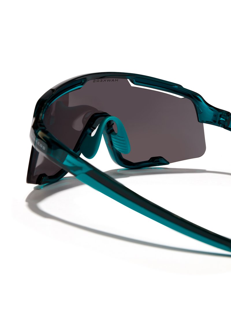 Sonnenbrille mit tealfarbenem Rahmen, grauen Gläsern und strukturierten Nasenpolstern. Das Design zeichnet sich durch markante Linien und eine aerodynamische Form aus.
