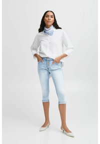 Camisa blanca de botones, jeans ajustados de color azul claro con cierre de botón en el frente, puños doblados y tacones de punta beige, accesorios con una bufanda azul.