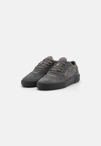 Adidași de skateboard din suede gri, cu un design low-profile, suprafață texturată și talpă din cauciuc. Şireturile și logo-ul lateral sunt într-o nuanță de gri asortată.