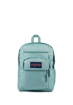 Mochila Jansport azul claro con tres compartimentos con cremallera y un bolsillo lateral de malla, mostrada sobre un fondo blanco.