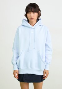 Sweatshirt azul claro com um bolso frontal, cordões ajustáveis e um pequeno logo da Nike em branco. Feito de material suave, possui punhos canelados.