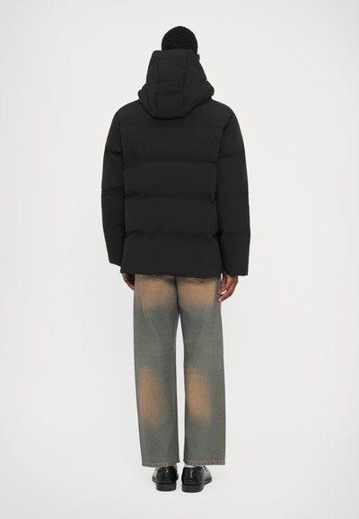 Black padded jacket with a hood, featuring a boxy shape and visible seams, paired with loose-fitting, faded denim jeans.