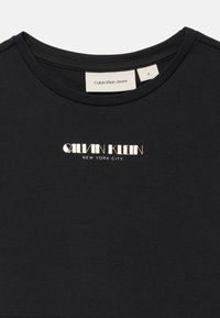 Melna kokvilnas t-kreklu ar apaļu kaklu, īsām piedurknēm un metālisku sudraba druku "Calvin Klein New York City" priekšpusē.