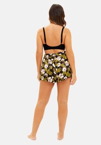 Brassière en dentelle noire avec des bretelles réglables, associée à un short à motifs avec un fond noir et un design floral blanc.