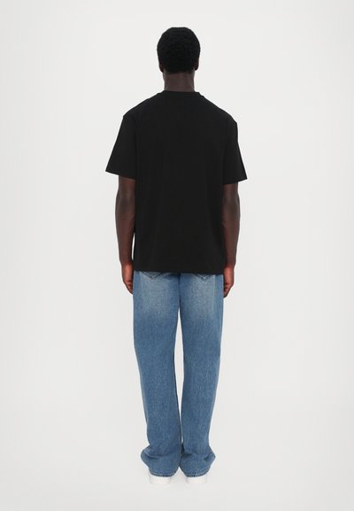 T-shirt noire à col rond associée à un jean en denim bleu clair à coupe décontractée, avec une texture lisse et une coupe droite.