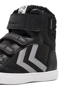 Sneaker alto nero realizzato in pelle e materiale sintetico. Presenta due chevron grigi, cinturini in Velcro e un rivestimento morbido e texturizzato.