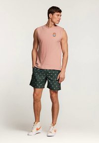Light pink sleeveless shirt with a small graphic, paired with green shorts featuring a palm tree pattern. White sneakers with orange accents.