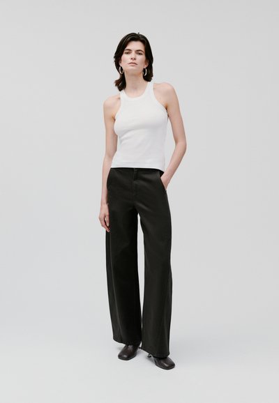 Top alb fără mâneci, asociat cu pantaloni negri cu talie înaltă și croială largă. Materialul pare neted, cu un design curat și minimalist.