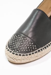 Espadrille de cuero negro con puntera con tachuelas, suela de yute y acentos de costura. La textura suave contrasta con las tachuelas texturizadas.