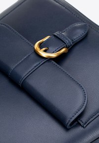 Granatowa skórzana torba z teksturowanym wykończeniem, z detalem w postaci zapięcia z złotym odcieniem i starannym szyciem wzdłuż krawędzi.