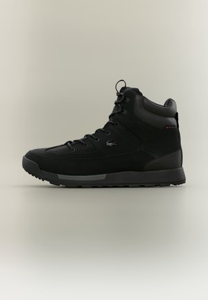 Black high-top sneaker with lace-up front, padded ankle collar, textured sole, and a small crocodile logo on the side.
