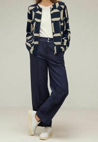 Námořnický a krémový kardigan s abstraktním vzorem, zkombinovaný s vysokým pasem námořnickými kalhotami a bílými teniskami. Hladká látka a přiléhavý střih.
