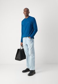 Blå langermet skjorte, lyseblå jeans, svarte lærersko og en strukturert svart totebag. Enkelt design med en avslappet passform.