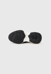 Semelle de basket noire et blanche avec des motifs de bande de roulement texturés pour une meilleure adhérence, affichée sur un fond gris clair uni.